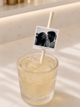 Load image into Gallery viewer, Black & white polaroid photo paper straw toppers on a drink garnished with ice in a vintage glass.