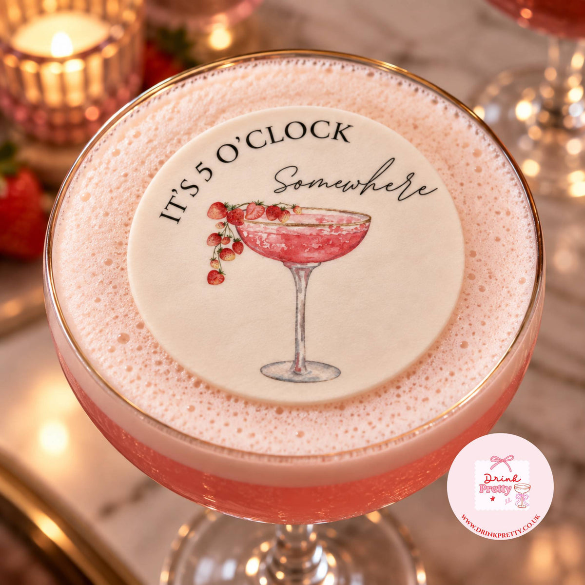 A pink cocktail in a coupe glass topped with thick foam and a round foam label reading 'IT'S 5 O'CLOCK Somewhere' with an illustration of a pink drink and berries. The photo is styled in a warm, candlelit environment with a small 'Dine With Pretty' logo in the bottom right corner.
