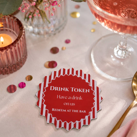 Red & white stripe drink tokens pack of 50 placed on a dining table with a drink and decorative elements.