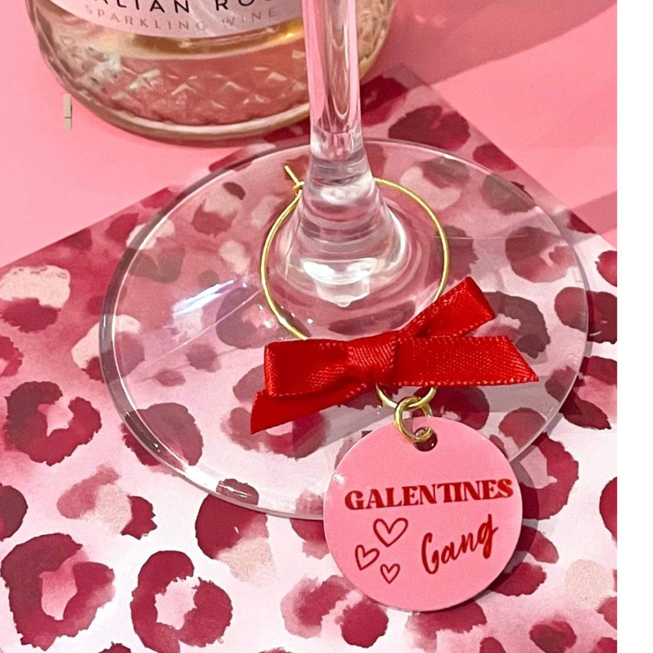 Wine glass with a 'Gal Valentines Gang' charm on a pink leopard print surface.
