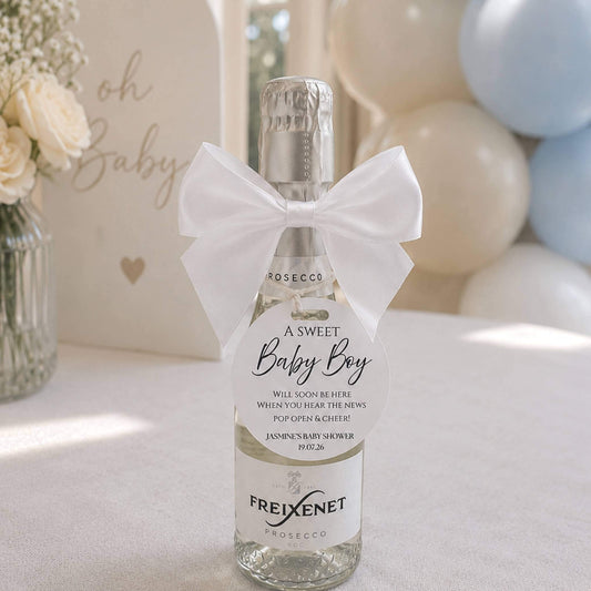 Baby shower pop the fizz bottle favour tags on a mini bottle of prosecco with a white bow for celebration.