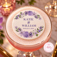 Load image into Gallery viewer, A close-up of a personalized round foam topper placed on top of a pink cocktail in a coupe glass. The topper is cream-colored with purple floral illustrations and the text 'KATIE & WILLIAM 18TH JULY 2025'.

