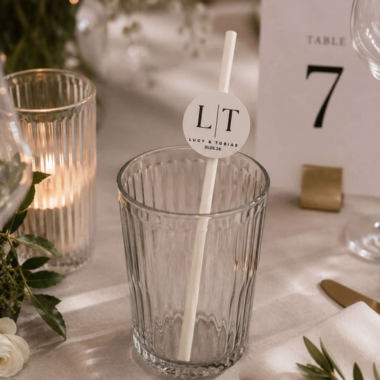 Occasion paper straws personalised initials toppers in a clear glass at a wedding table setting.