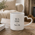 Load image into Gallery viewer, Personalised tea time mug with heart-shaped handle on a wooden table.
