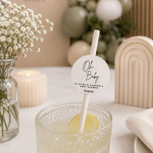 Oh Baby Personalised paper straw toppers in a drink at a baby shower with floral decor and soft colors.