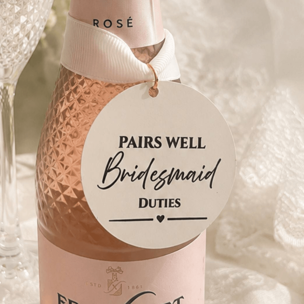 Wedding Pairs Well with bottle charm tag on a bottle of rosé, featuring a tag that reads 'Pairs Well Bridesmaid Duties'.