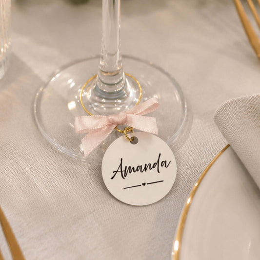 Personalised name wine glass charms with a name tag and pink bow on a wine glass.