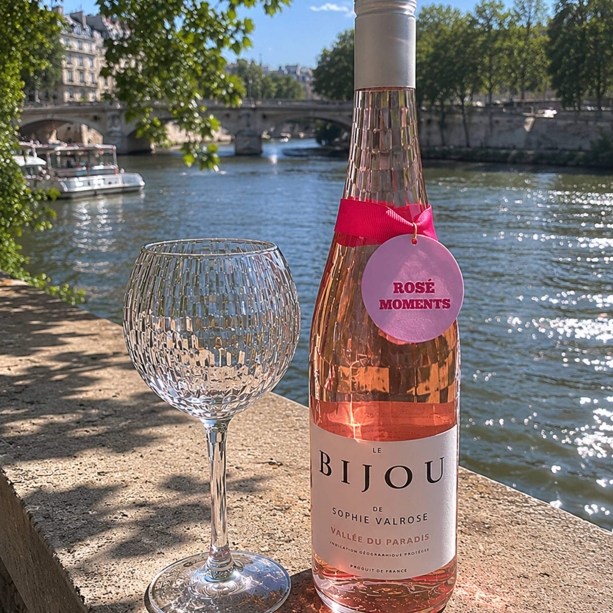 Rose Moments Bottle Charm Gift Tag on a bottle of rosé wine by the river with a crystal glass.