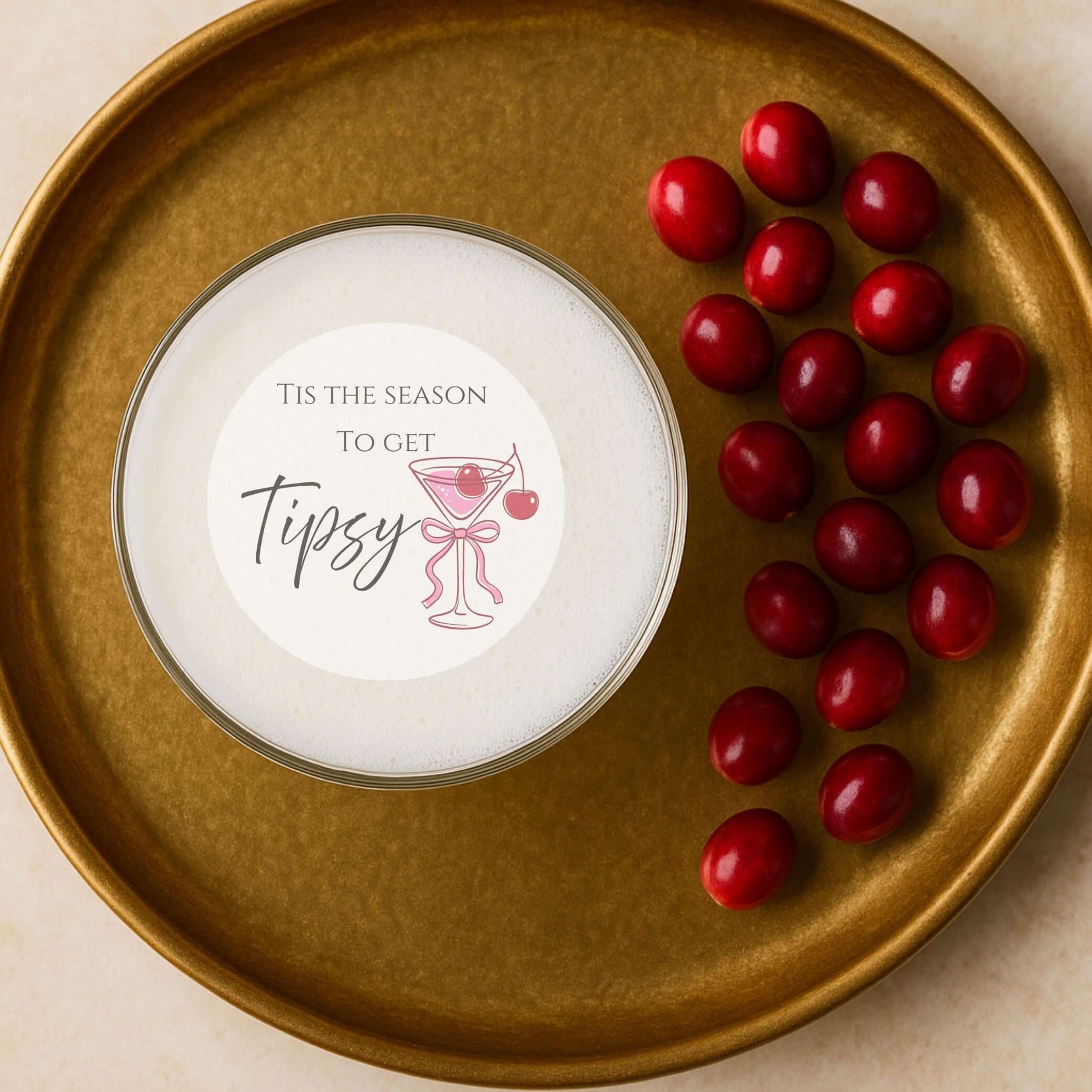Tis The Season To Get Tipsy edible drink topper on a gold plate with cranberries for stylish holiday cocktails.