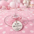 Load image into Gallery viewer, Wine glass with a baby shower tag on a pink polka dot background
